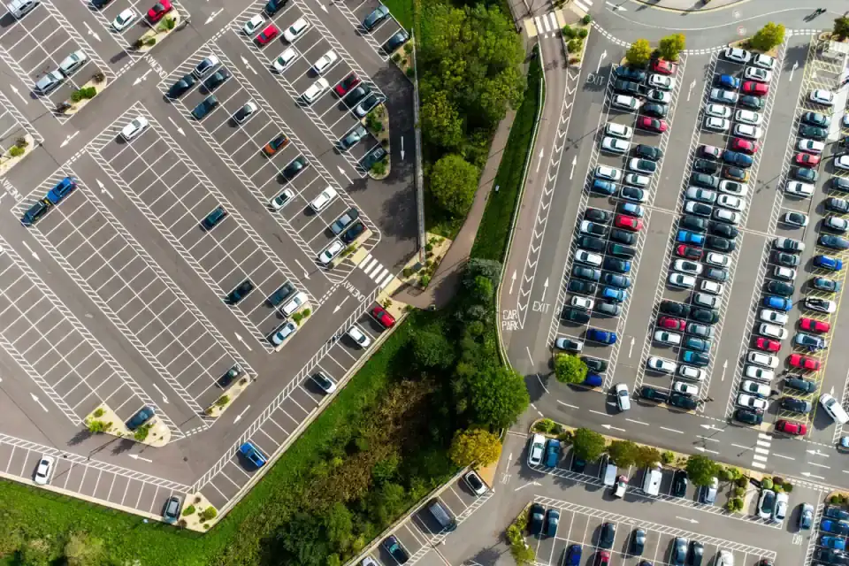 Aerial view of large parking lots filled with rows of cars beside green landscaping