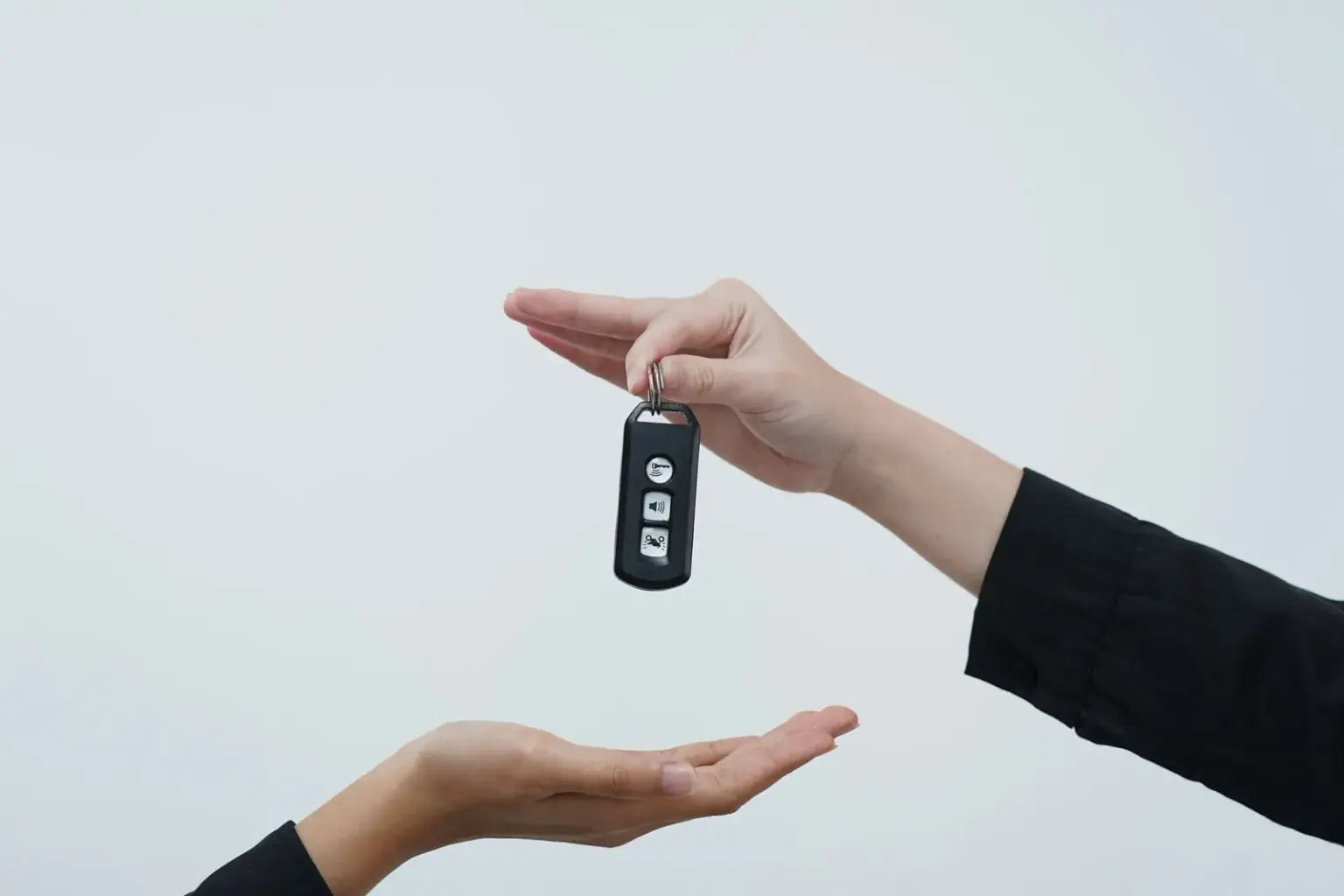 One person handing a car key fob to another person's open hand against a light background