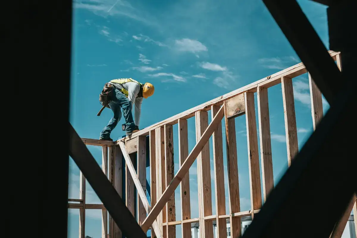Construction worker in a hard hat and safety vest working on top of timber wall framing