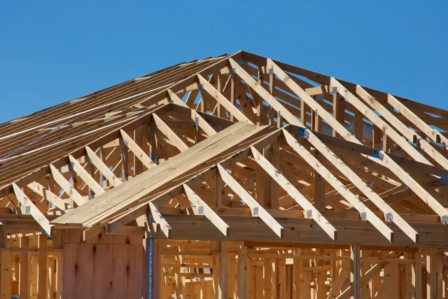 Wooden roof trusses and wall framing of a house under construction against a blue sky