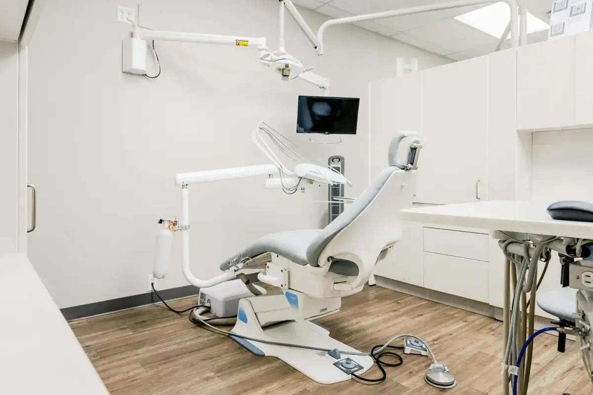 Empty dental operatory with a gray patient chair, wall-mounted monitor and wood-look floor