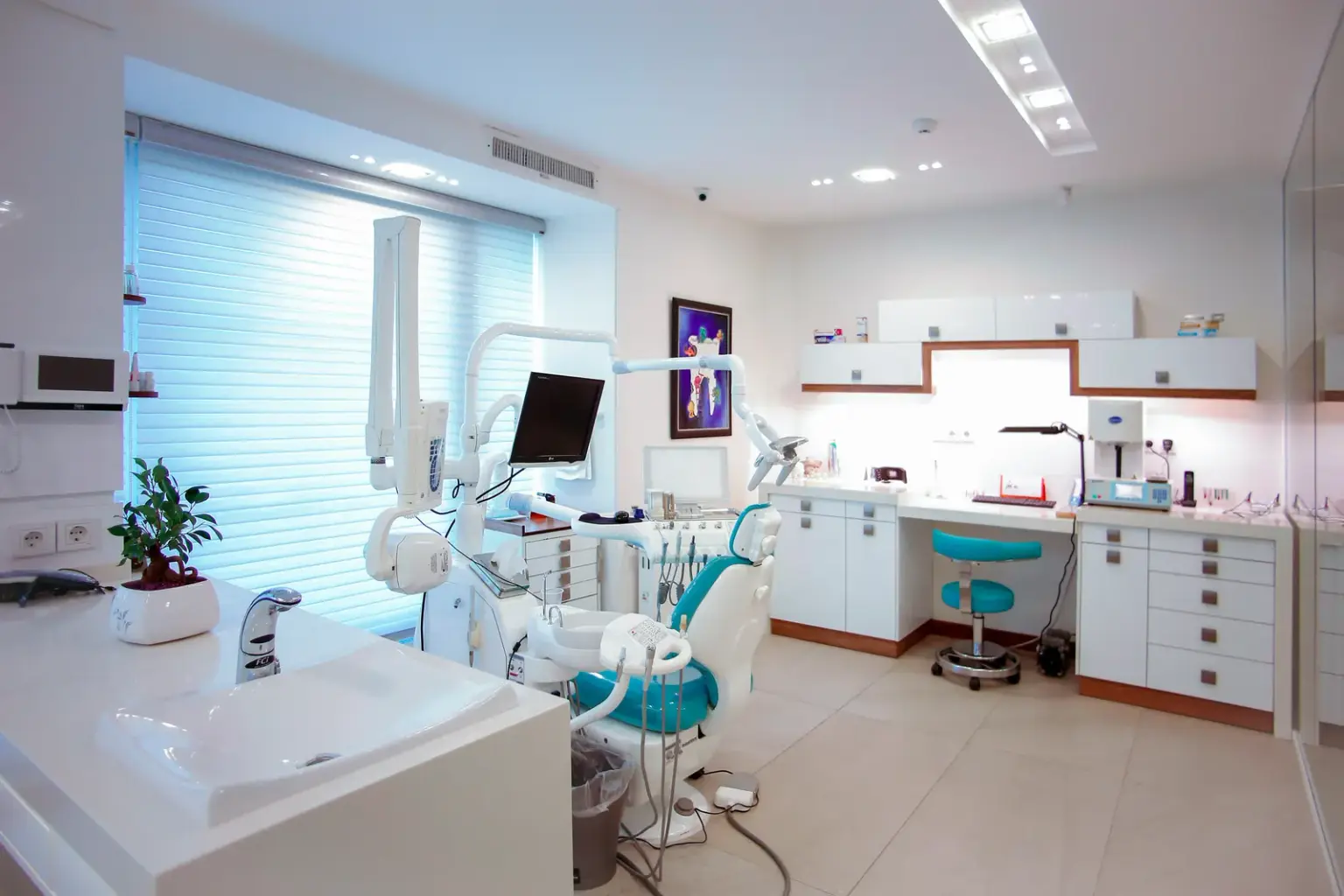Bright modern dental treatment room with a patient chair, overhead light, monitor and white cabinetry