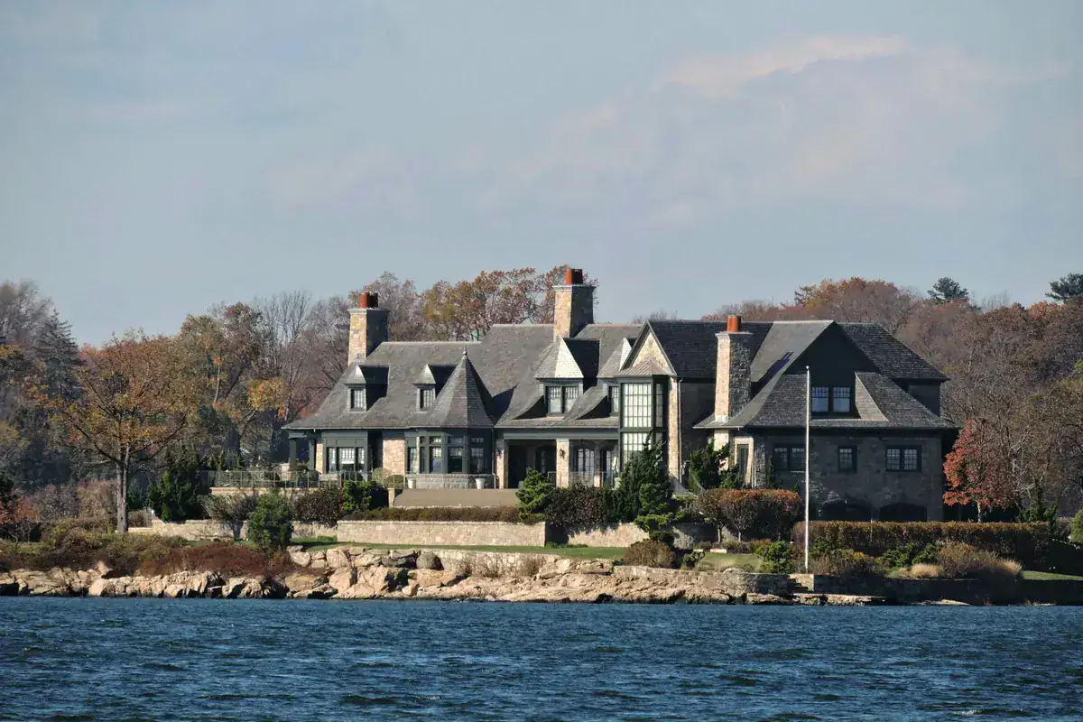 Large waterfront house with gabled roofs and stone chimneys on the Greenwich, Connecticut shoreline in autumn