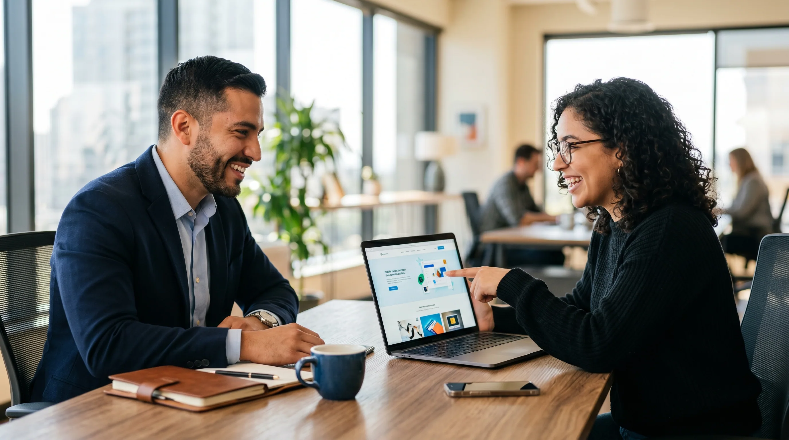 Two people smiling as one presents a website on a laptop at an office table